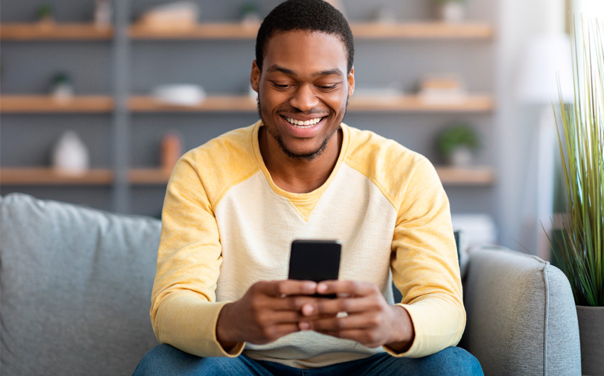 Um homem sorri relaxado enquanto acessa serviços digitalizados em seu smartphone